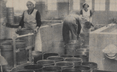 300257 Afbeelding van het met heet water spoelen van de akers (emmers) in het nieuwe gebouw van de Centrale Keuken ...